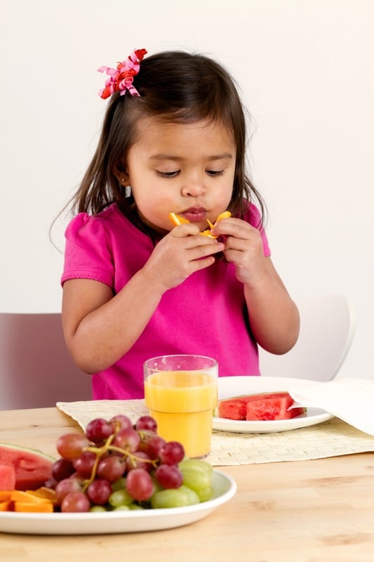 Little child sitting at a table, eating and practicing table manners